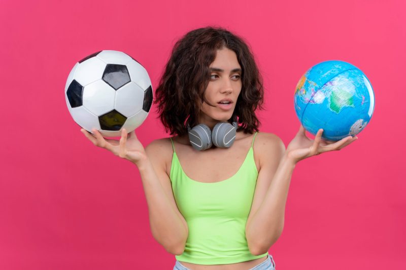 young-pretty-woman-with-short-hair-green-crop-top-headphones-holding-globe-soccer-ball